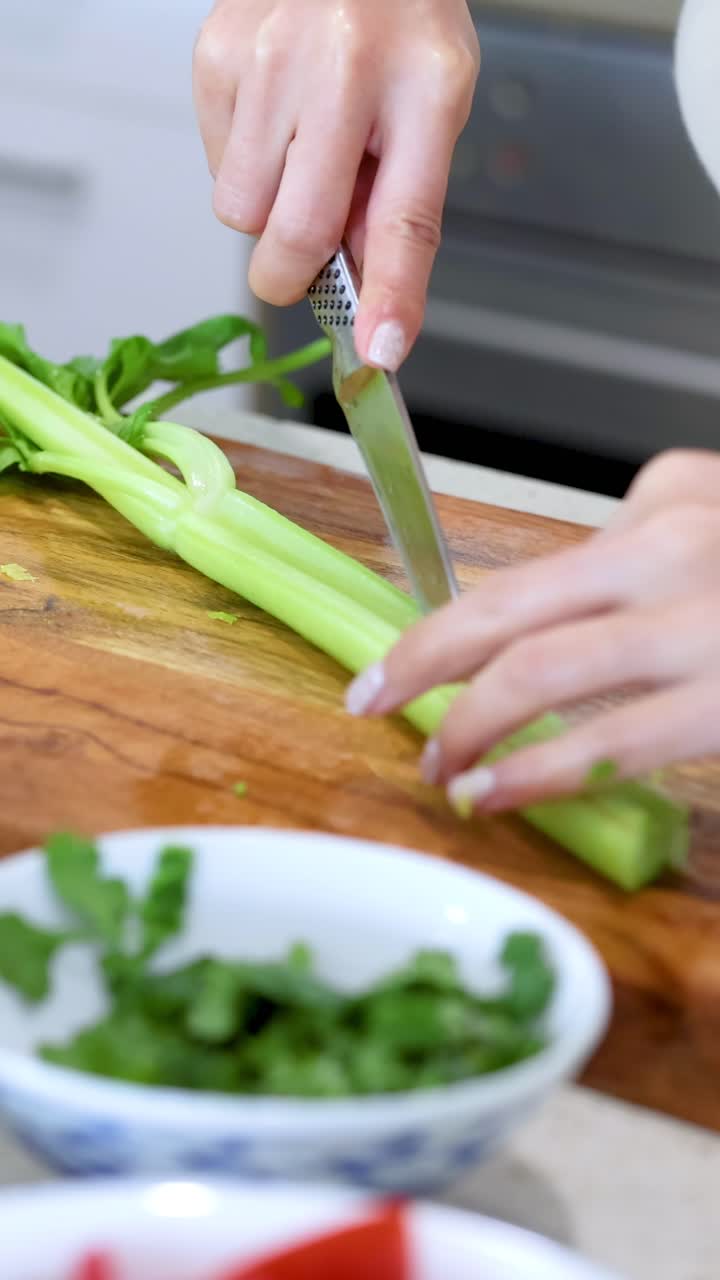 Una persona affetta sedano su un tagliere di legno in una cucina luminosa, mettendo in risalto l'abilità precisa nel taglio e gli ingredienti freschi.