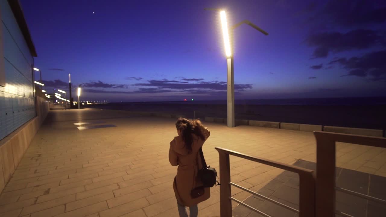 mujer caminando por el paseo marítimo de la playa al atardecer en cámara lenta