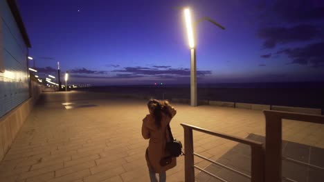 woman walking along the promenade on the beach at dusk in slow motion