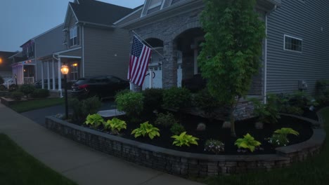 suburban neighborhood house with american flag on porch. foggy evening light emphasizes residential details. aerial rising shot.