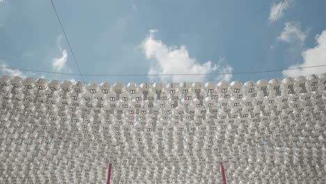 Rows-of-White-Color-Rounded-Pater-Lanterns-with-Blessing-Cards-Hanging-on-Lines-for-Decoration-Against-Blue-Sky-in-Buddhist-Temple