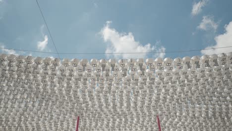 filas de farolillos de pater redondeados de color blanco con tarjetas de bendición colgando de las líneas para la decoración contra el cielo azul en el templo budista