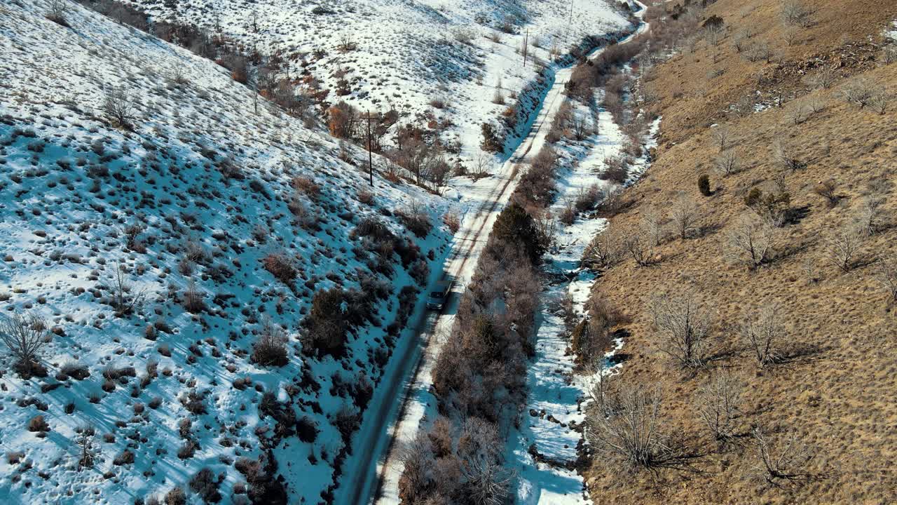 A truck driving through a narrow canyon on a dirt road with snow on the north facing slope