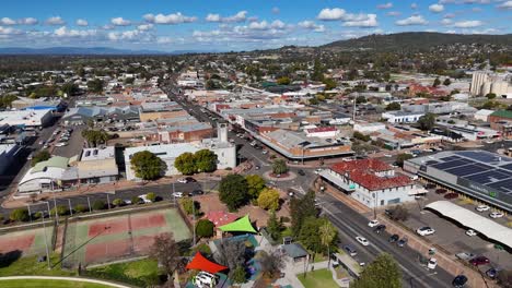 drone camera glides above glen innes, nsw, revealing city streets, parked cars, and commercial buildings under bright daylight with clear skies