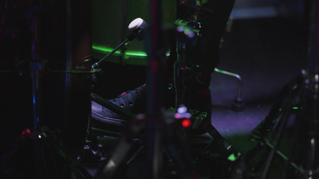 Primo piano del piede di un batterista che usa il pedale della grancassa su una batteria, su un palco illuminato e multicolore
