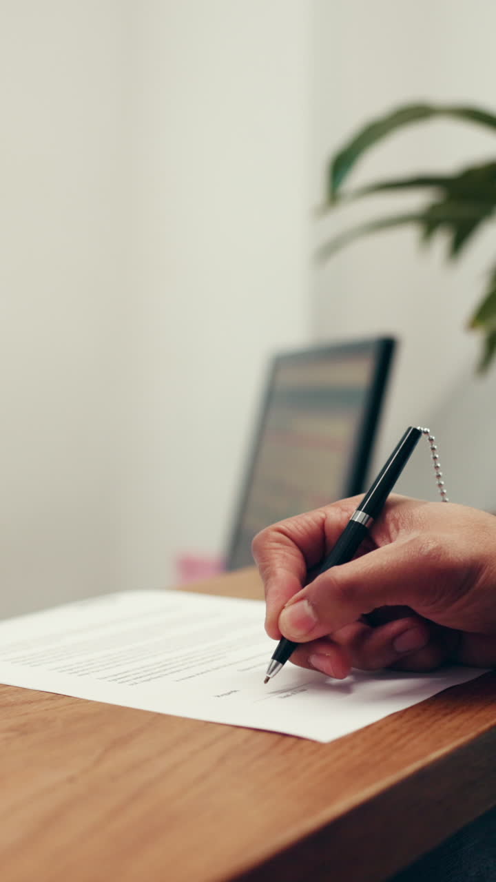 Primo piano di una mano che firma un documento con una penna sulla scrivania