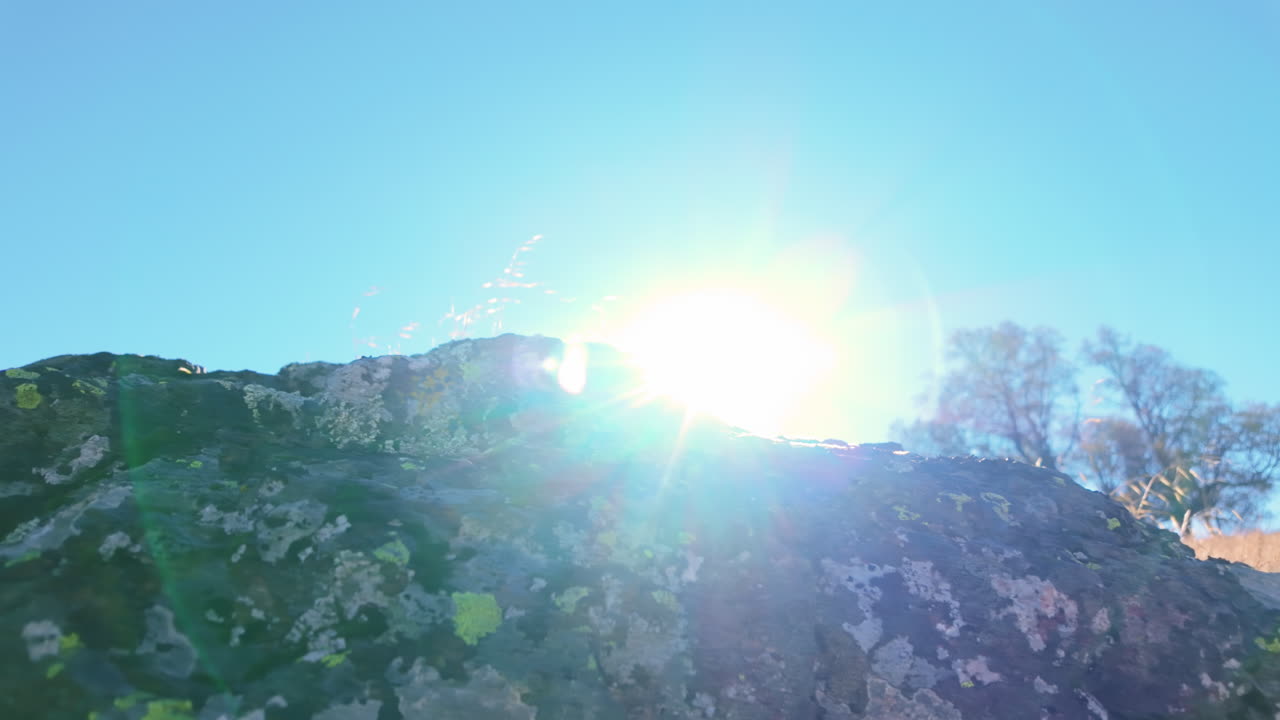 Helle Sonne, die hinter einem moosbewachsenen Felsen mit Lens Flare aufgeht.