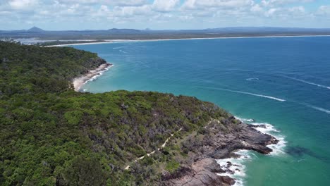 dron descendiendo sobre una península que muestra una playa rocosa debajo