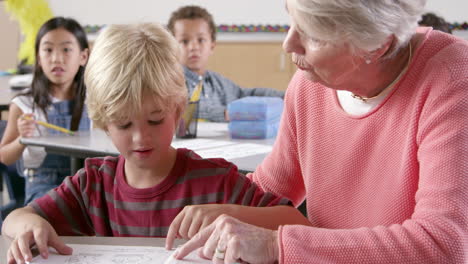 senior female teacher helps young schoolboy reading in class