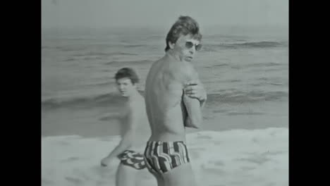 men standing on a beach by the ocean, enjoying the view. circa ussr 1980s: men standing atop a beach next to the ocean, taking in the picturesque scenery.
