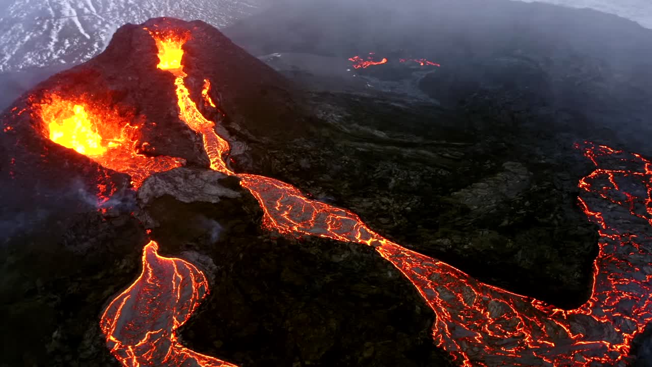 Riprese aeree cinematografiche catturate da un drone 4K mostrano la vista unica di due vulcani posizionati fianco a fianco, entrambi che espellono lava rapidamente mentre fiumi di lava fusa scendono a cascata.