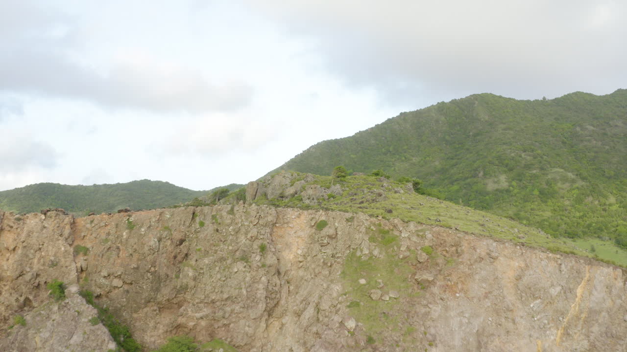Early morning, smooth fly in, towards and past cliffside onto mountainous terrain coved in lush green foliage.4K UHD at 23.98 fps