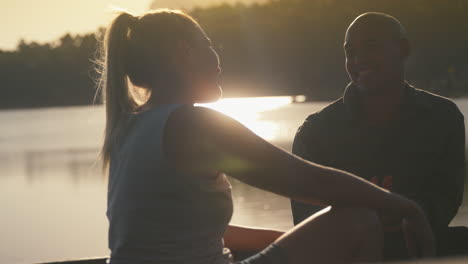 couple sitting in back of pick up truck on road trip by lake at sunset