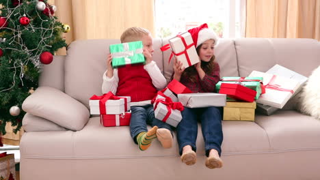 cute siblings sitting on couch with lots of christmas gifts