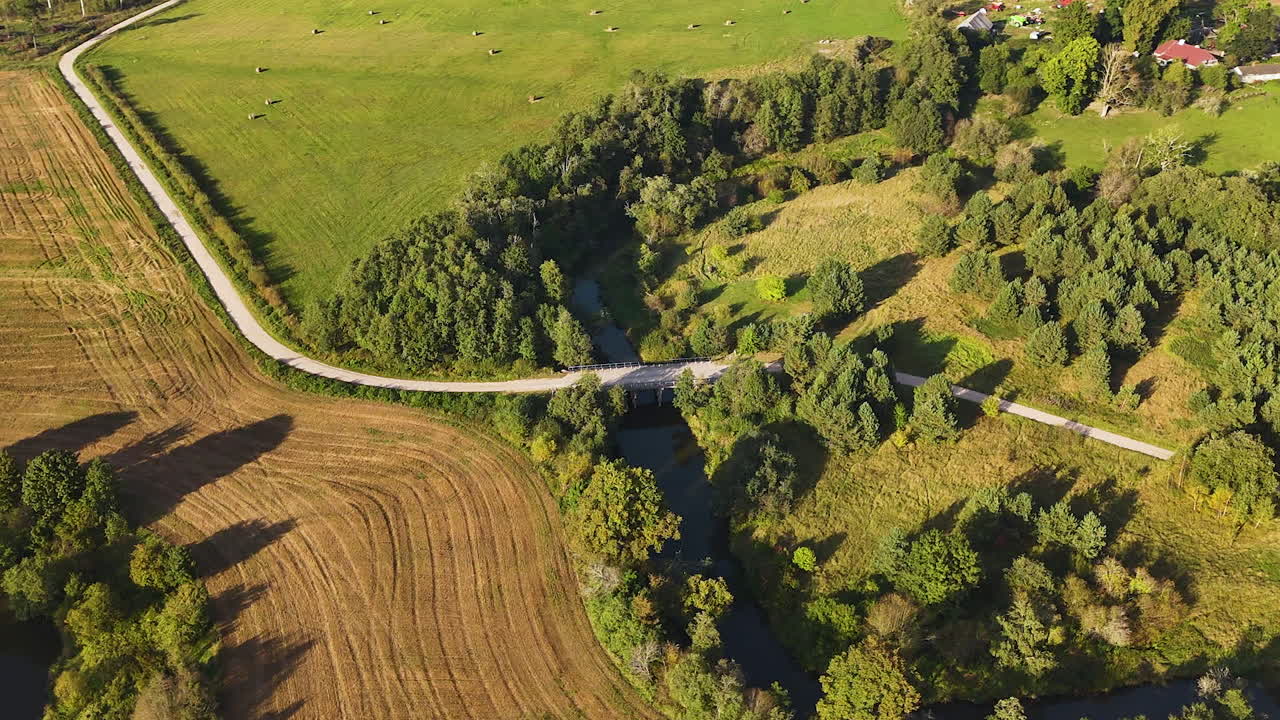Bridge over the Tebra river with forested and cultivated fields in rural Latvia.