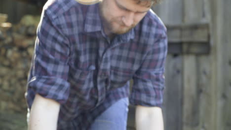 man picks up logs from pile and sets it on a stack