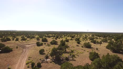 Aerial-flyover-dirt-road-crosses-the-Grand-Canyon-Railroad-over-open-range,-ponderosa-pine-forest,-and-wind-farm-just-north-of-Williams,-Arizona