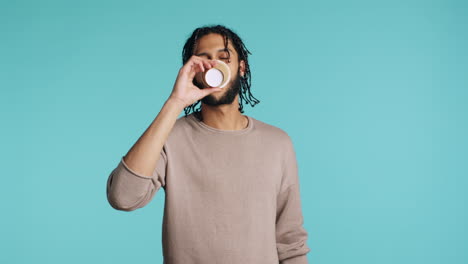 Man-enjoying-fresh-coffee-from-disposable-paper-cup,-studio-background