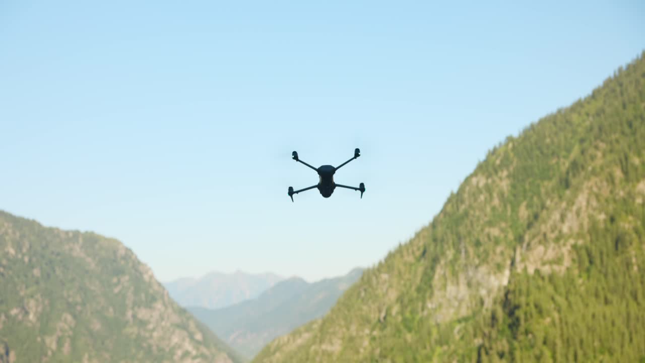 A drone navigating between mountains under clear skies, showcasing aerial technology and nature