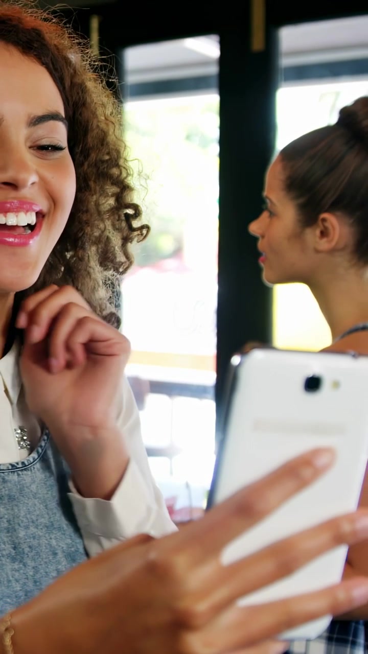 Video verticale: Donna riccia che posa con il telefono, avviando sovrapposizioni in AR che collegano viso e telefono per annunci pubblicitari.