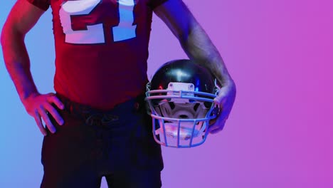 video of midsection of caucasian american football player with helmet over neon purple background