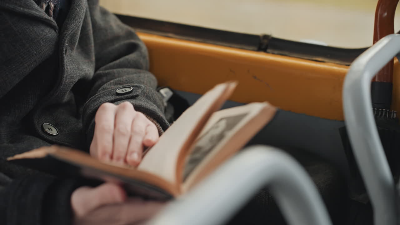 Eine Person, tief in ein Buch vertieft während einer Reise. Die Person konzentriert sich auf das Lesen, während sie in einem friedlichen Bus reist. Ein Mann widmet sich seinem Buch, während er in der Herbstzeit ruhig fährt