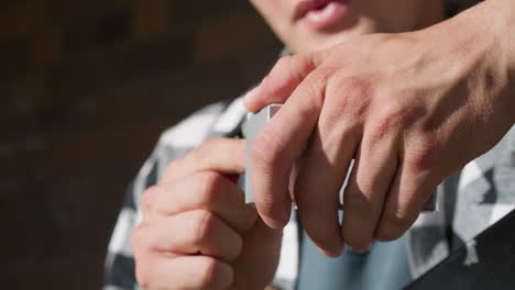 close up of smoker retrieving cigarette from pack while gripping lighter and placing tip in mouth ready to ignite, fingers pressing flint and metal rail brick wall casting soft urban shadows around