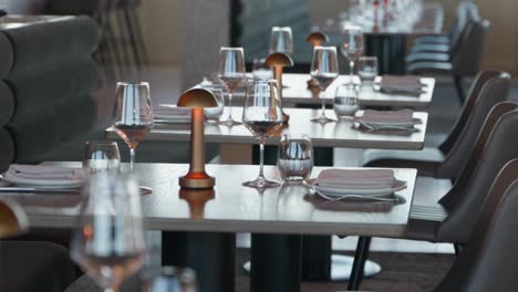 elegant tables and seating in a fine dining restaurant with fancy tableware, wine and water glasses and silverware with a decorative romantic dim lamp in the centre
