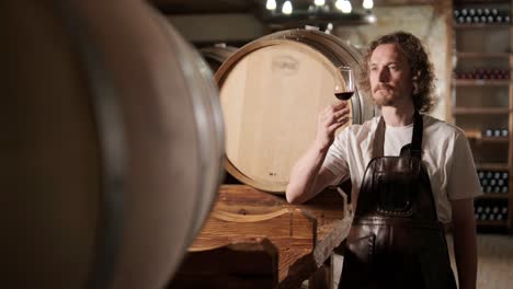 authentic shot of successful male sommelier is tasting a flavor and checking white wine quality poured in transparent glass in a wine cellar.