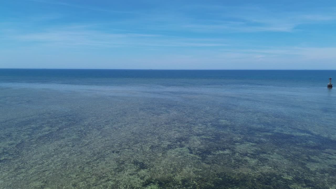 Drone pans left and advances slowly over the clear shallow waters of My Hoa Lagoon, with the horizon and coastal mountains visible.