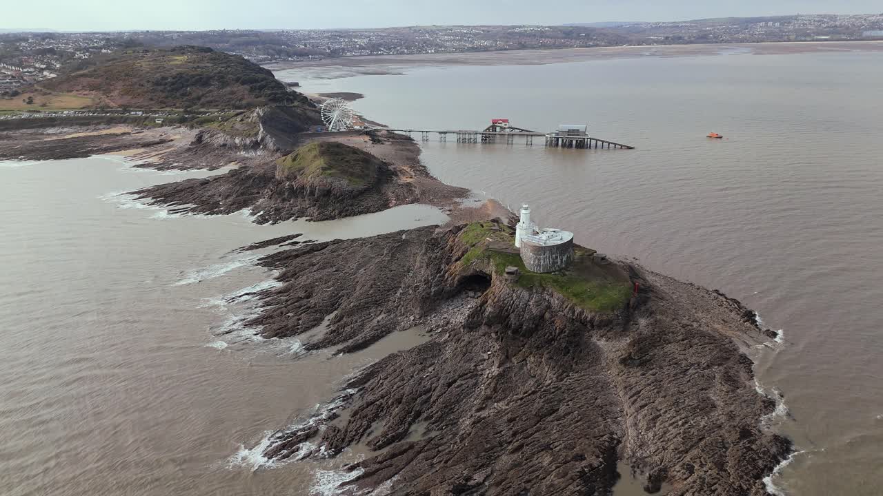 Forward moving drone shot of Mumbles Lighthouse near Swansea with the Big wheel at background in England.