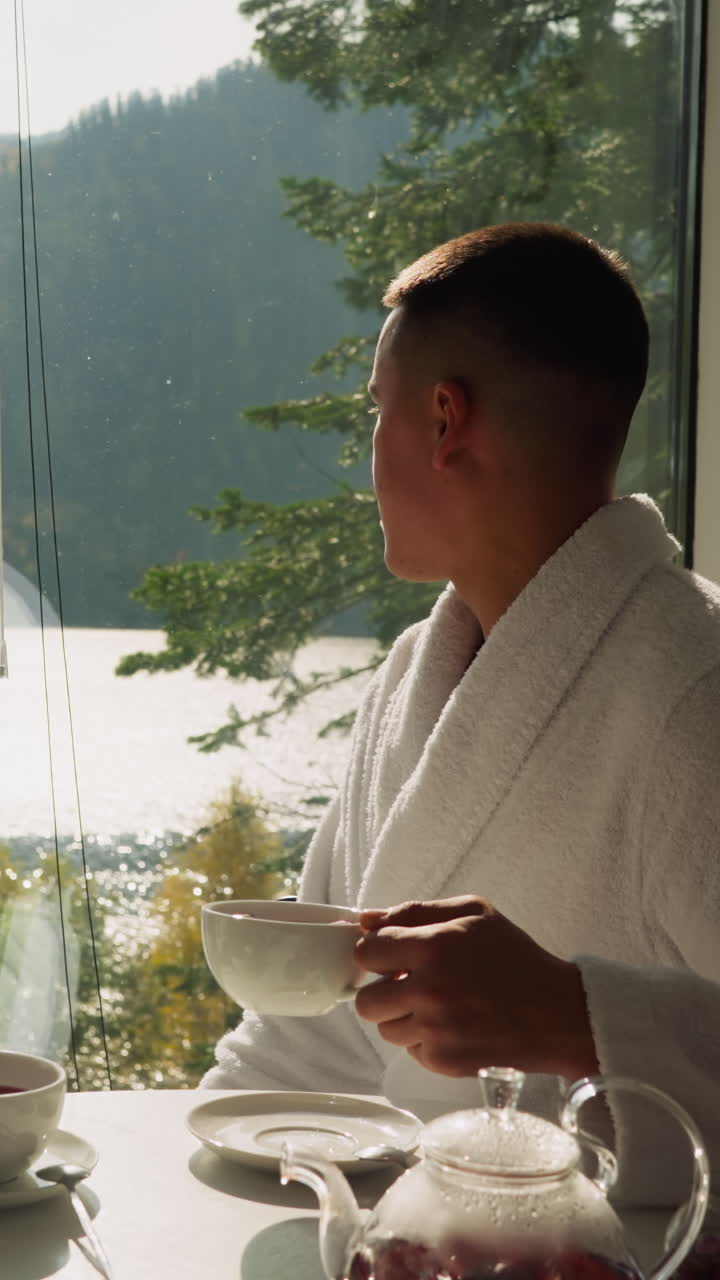 신혼부부는 창문으로 바라보는 자연을 감상합니다. 테리 목욕복을 입은 부부는 글램핑 호텔에서 향신료 차를 즐니다. 야생 자연 지역에서 럭셔리 주말의 개념