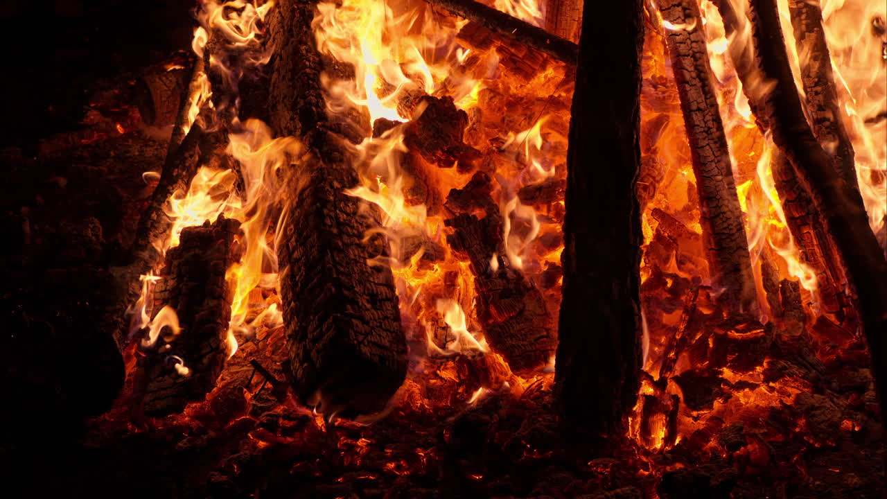 Close up of wood burning in a bonfire at night with a distant view of the mood on the background