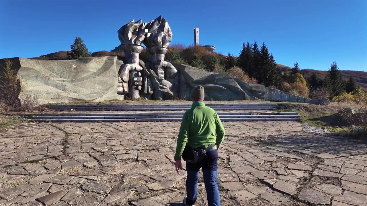 Escursionista che cammina verso le gigantesche mani di pietra che reggono torce al Monumento di Buzludzha sui monti Balcani in Bulgaria