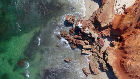 Wellen,-Die-Gegen-Roten-Felsen-Am-Strand-Schlagen