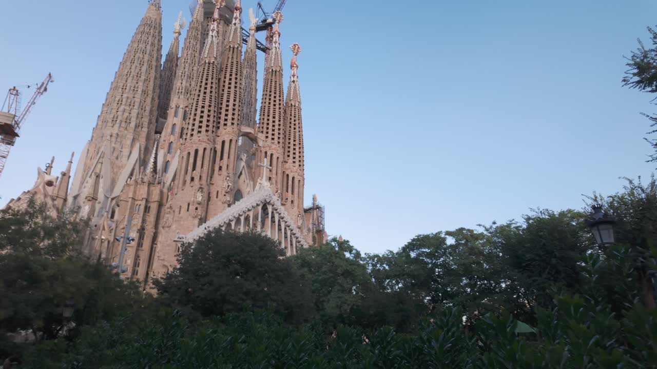 Iconic La Sagrada Familia basilica with construction cranes and trees in Barcelona Spain