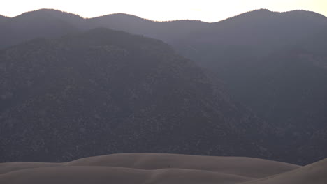persona diminuta caminando sobre dunas de arena con enormes montañas en segundo plano.