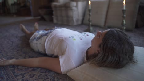 young latin female meditating ritual with candles lying on the floor in a wooden home slow motion and 60fps