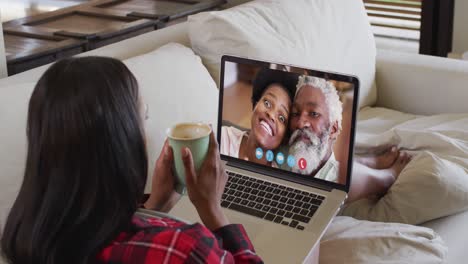 Mujer-Afroamericana-Sosteniendo-Una-Taza-De-Café-Con-Una-Videollamada-En-Una-Computadora-Portátil-Sentada-En-El-Sofá-En-Casa