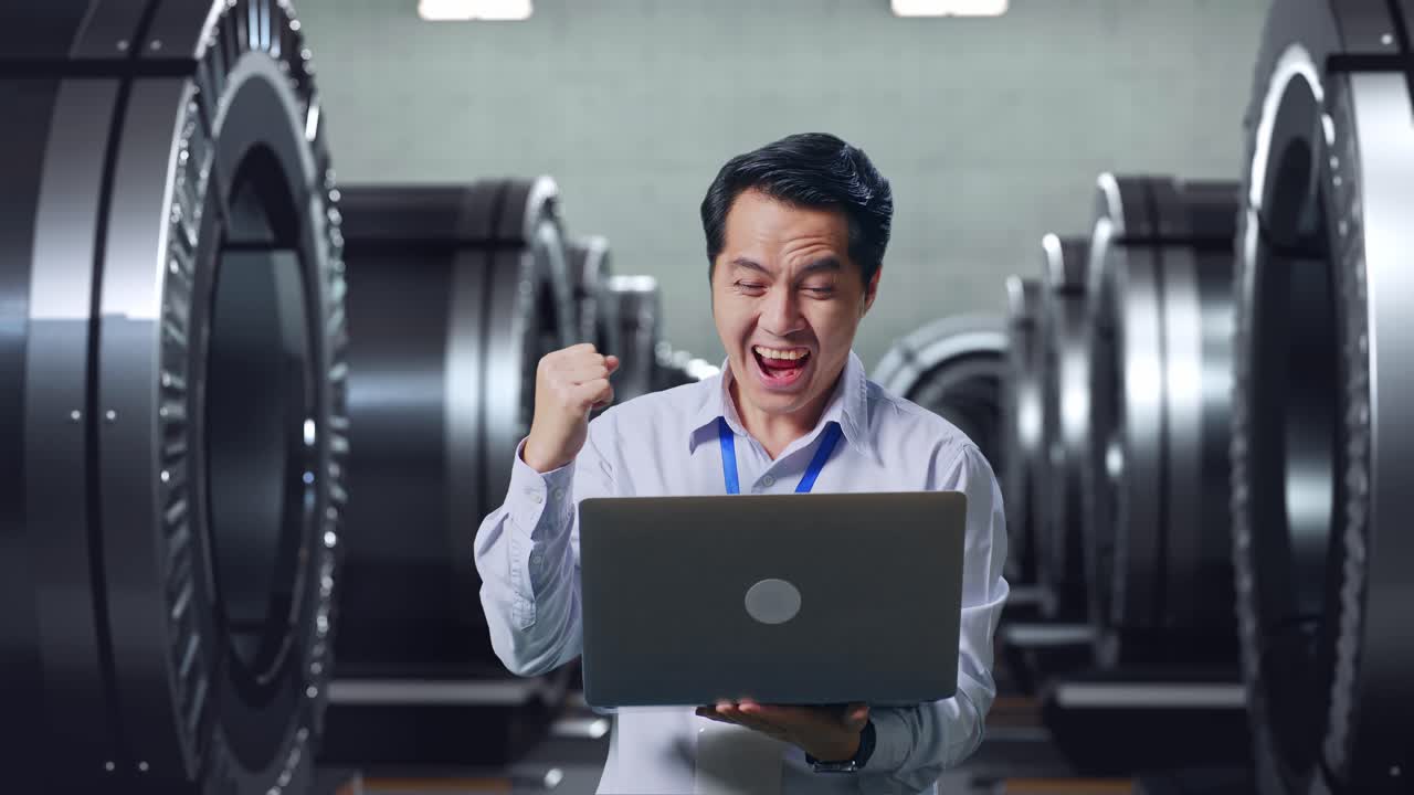 행복한 엔지니어가 공장에서 노트북으로 성공을 축하하고 있습니다.