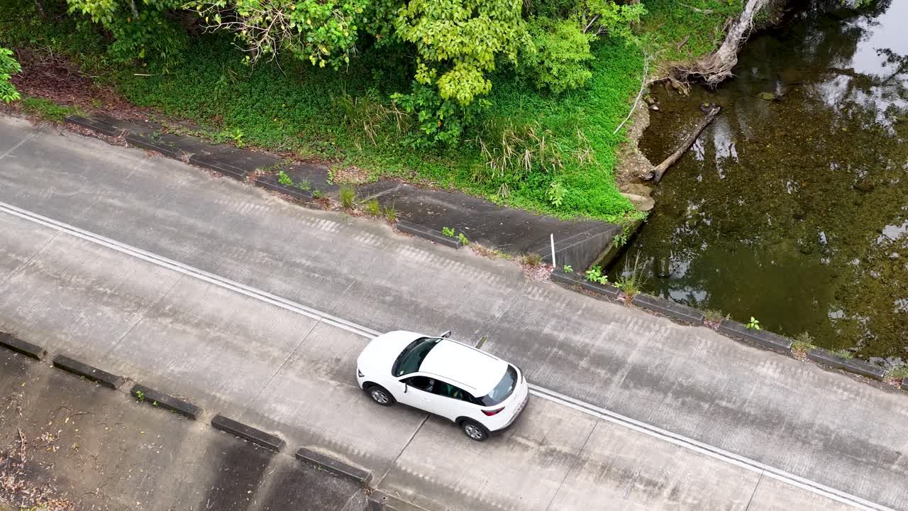 Aerial footage captures a car crossing a bridge surrounded by lush rainforest in Port Douglas, Australia. Bright, natural lighting enhances the scene