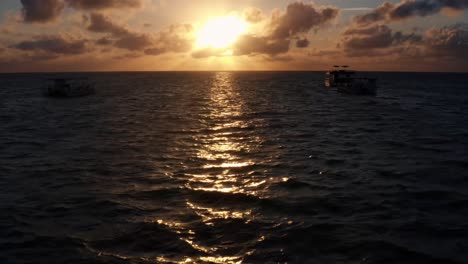 hermosa toma aérea de drones inclinados hacia arriba de un amanecer en el océano en la playa bien cerca de joao pessoa en una cálida mañana de verano con el agua debajo, nubes doradas en el horizonte y pequeños botes en el agua