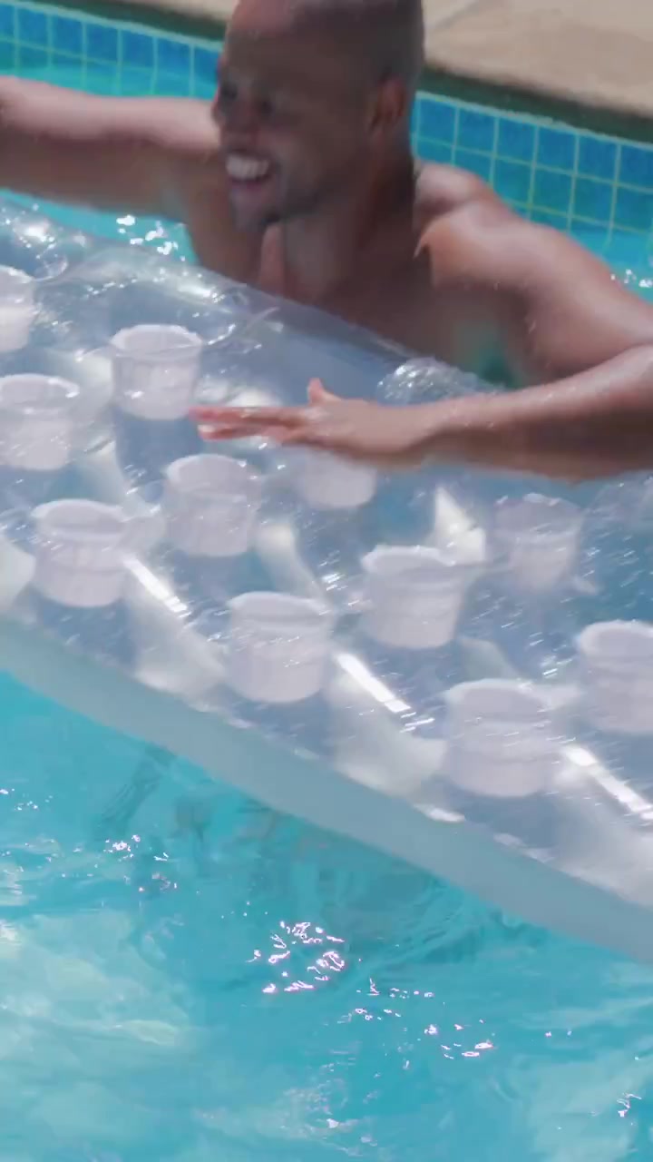 Vertical video: Lifting dad in trunks pushing float climbing onto it in pool kid in trunks holding
