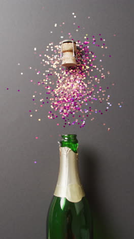 video vertical de una botella de champán y un corcho explotante con brillos rosados y dorados de colores