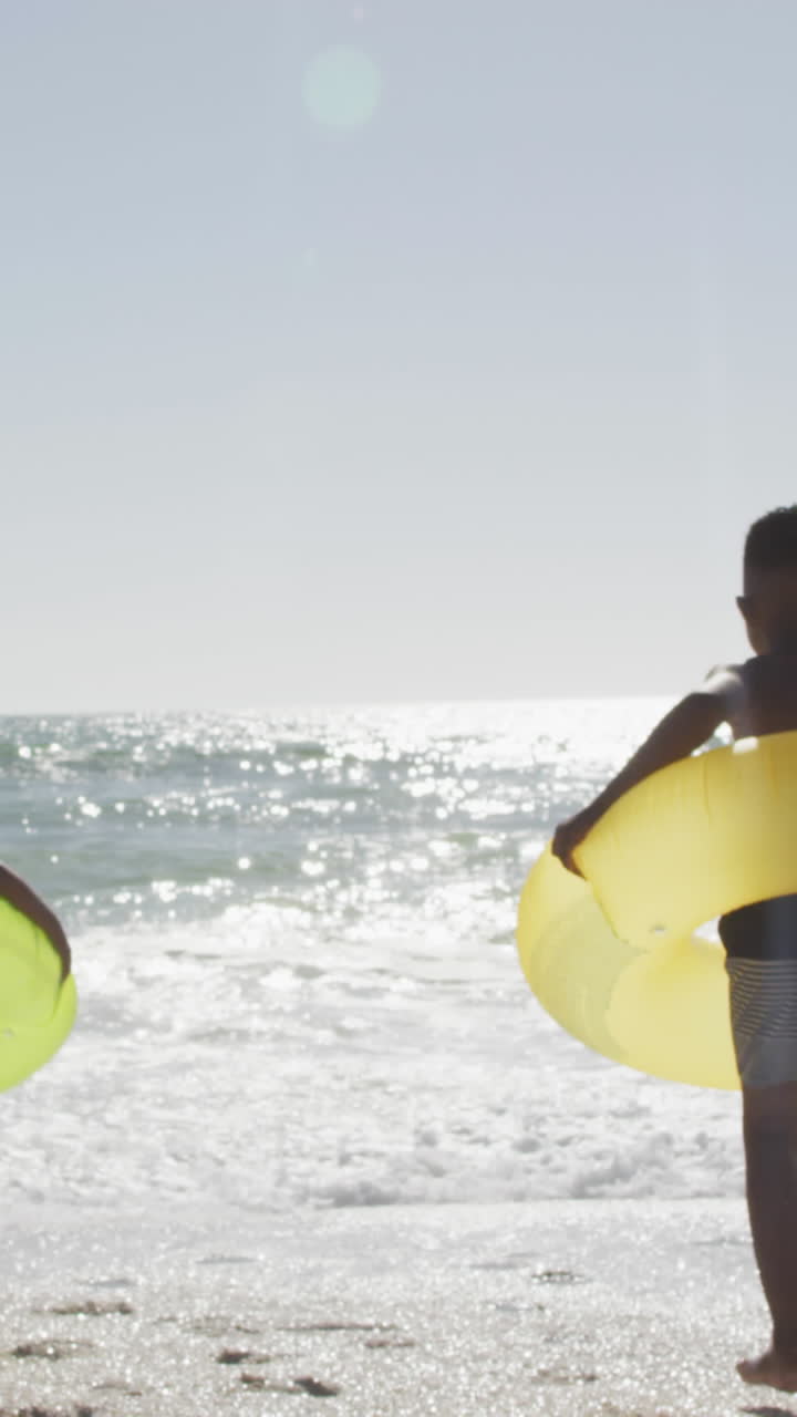 familia afroamericana con inflables corriendo hacia el agua en una playa soleada