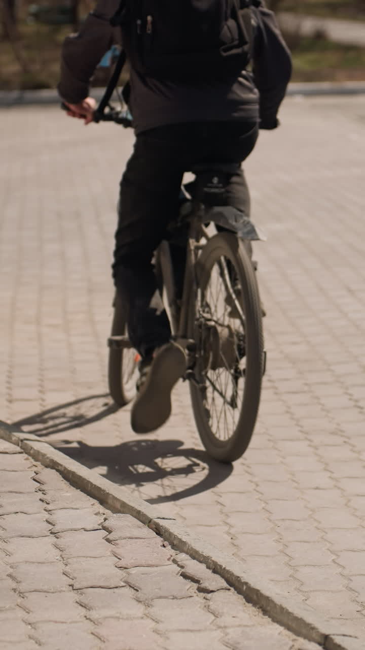 Close view of a cyclist standing beside a bicycle on a paved path to ride, the rider is wearing a jacket and jeans, with the shadow of the bike cast on the ground
