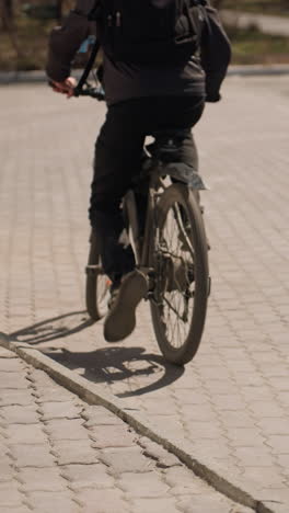 vista ravvicinata di un ciclista in piedi accanto a una bicicletta su un sentiero asfaltato per cavalcare, il ciclista indossa una giacca e jeans, con l'ombra della bicicletta lanciata sul terreno