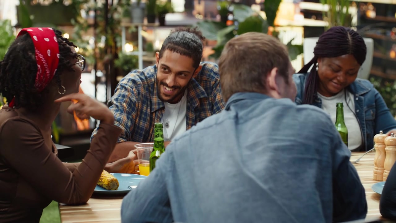Group of friends talking and laughing across rooftop dining table
