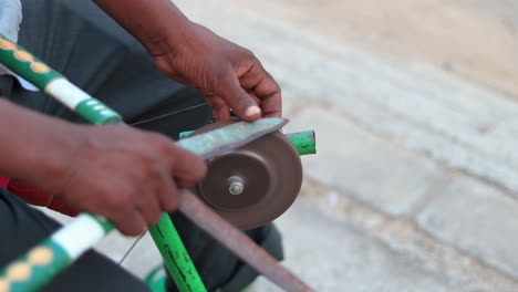 hombre de primer plano afilando tijeras de jardinería en una máquina afiladora móvil improvisada en un marco de bicicleta manual