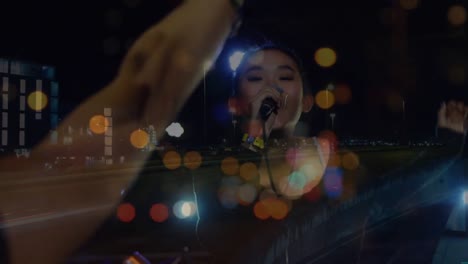 Animation-of-blurred-night-road-traffic-over-happy-asian-female-singer-on-concert
